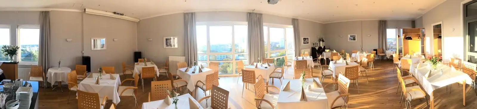 Eingedeckte Tische im Caféraum mit warmem Sonnenlicht und Fensterblick.