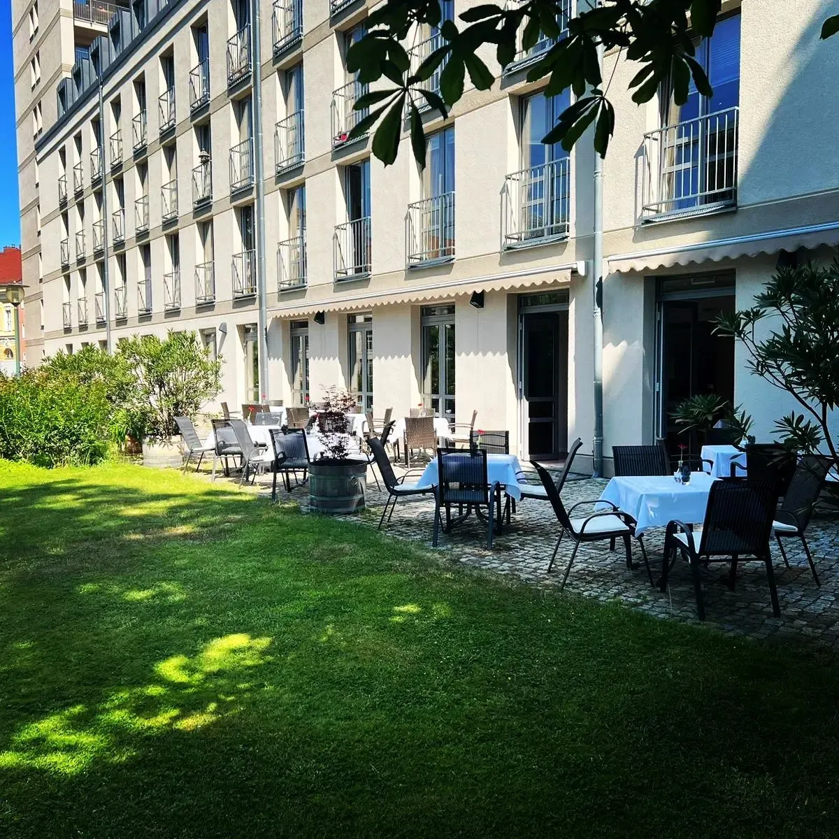 Terrasse mit gedeckten Tischen, Rasen und sommerlichem Hof.