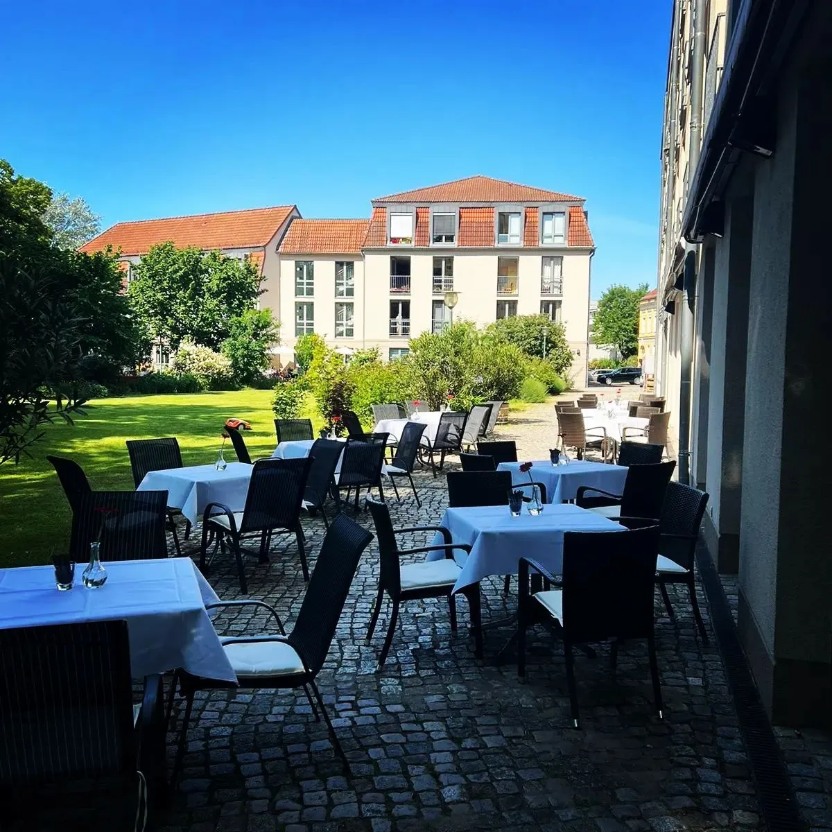Sonnige Terrasse mit eingedeckten Tischen, Pflaster und Hofblick.